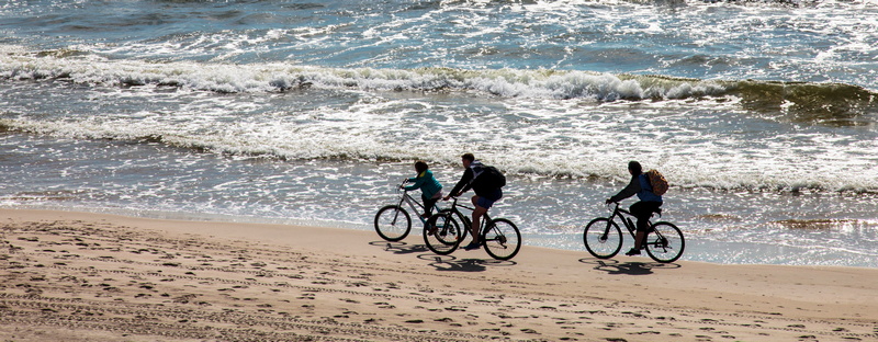 3 osoby na rowerze na plaży nad morzem