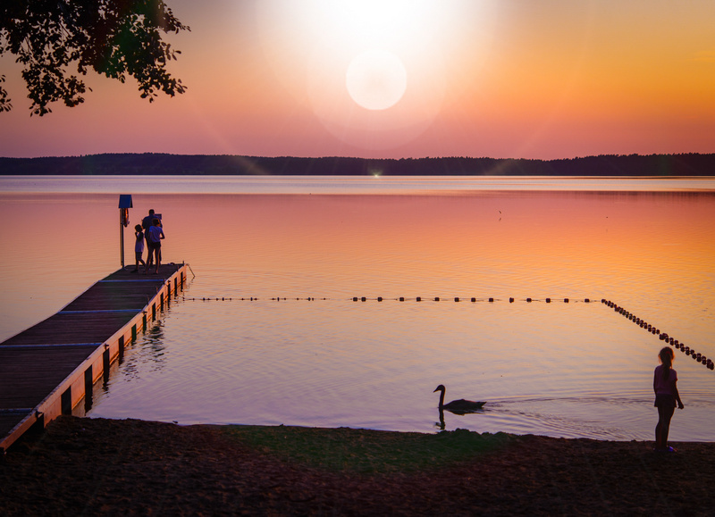 Ludzie na plaży nad jeziorem o zachodzie słońca