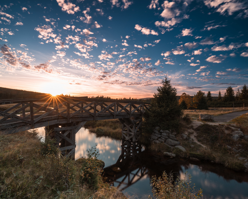 Mostek nad potokiem na tle zachodzącego słońca