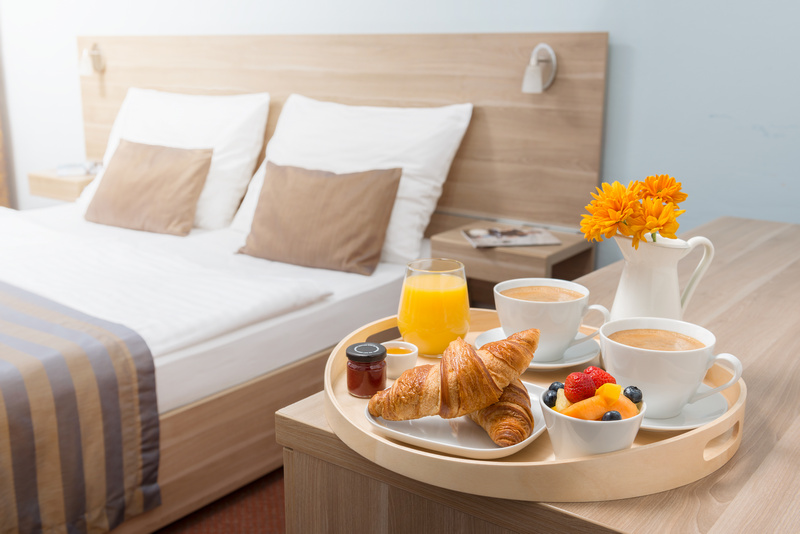 Taca ze śniadaniem postawiona obok łóżka w pokoju hotelowym
