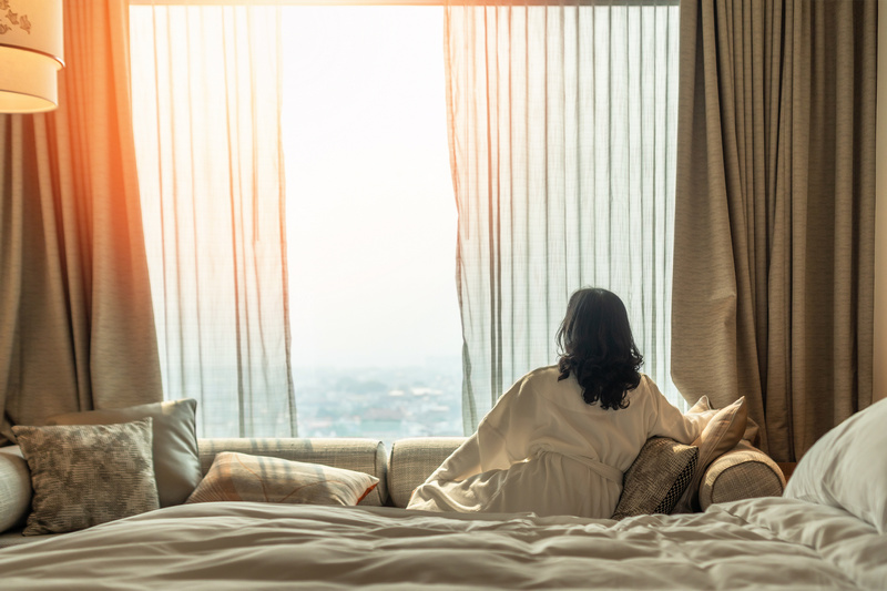 Kobieta siedząca na hotelowym łóżku i patrząca przez okno