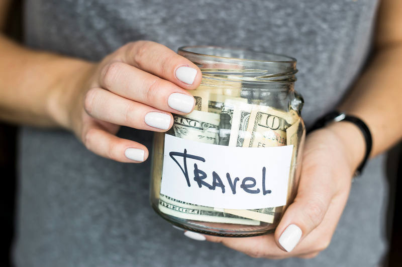Kobieta trzymająca słoik z napisem travel z pieniędzmi w środku.