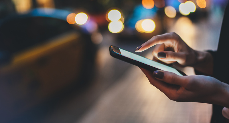 Kobieta trzymająca telefon na tle rozmytych miejskich świateł