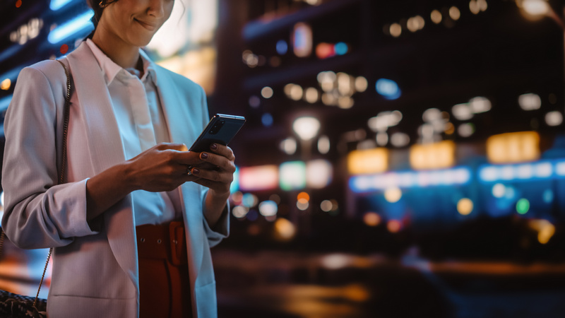 Kobieta w mieście nocą sprawdzająca coś na telefonie