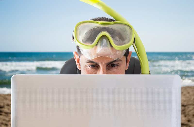 Mężczyzna z maską do nurkowania przed laptopem z morzem w tle
