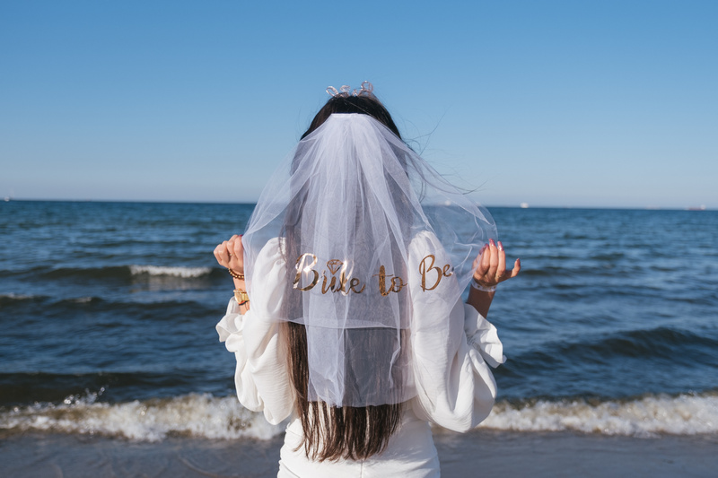 Dziewczyna stojąca tyłem z welonem z napisem bride to be na tle Bałtyku