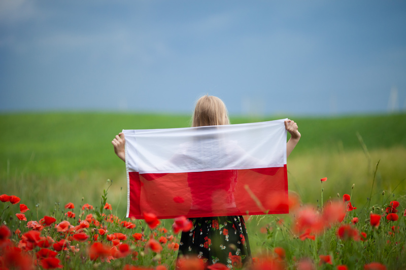 Dziewczynka w polu maków trzymająca rozciągniętą flagę Polski