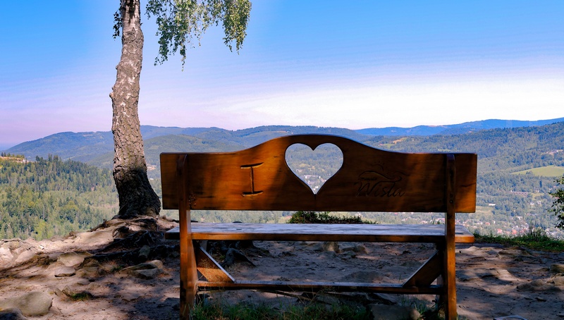 Ławka z wyciętym sercem w oparciu, przez które widać górskie miasteczko
