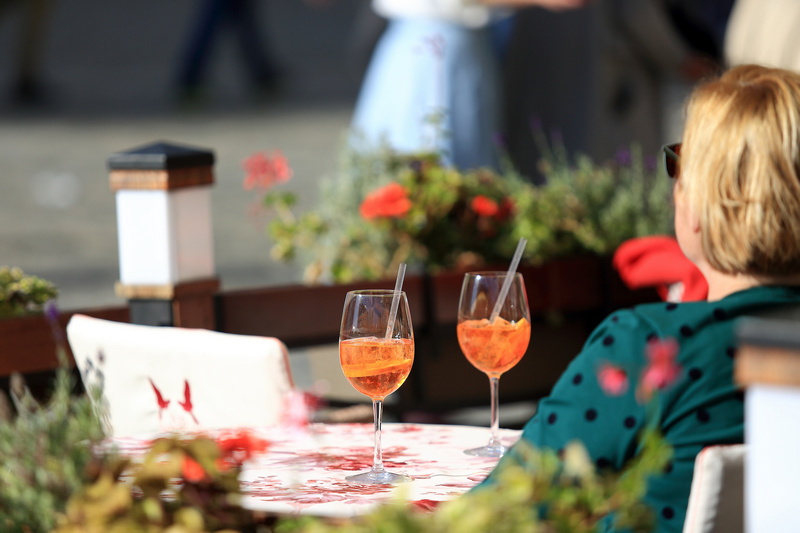 Kobieta siedząca przy stoliku z dwoma kieliszkami z pomarańczowym napojem i rurkami
