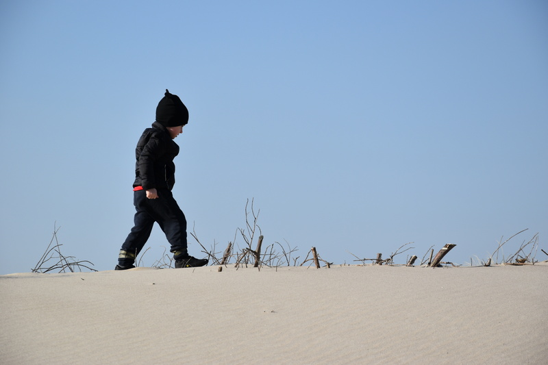 Chłopiec w zimowej czapce chodzący po wydmach nad morzem