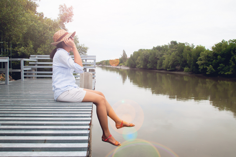 Kobieta siedząca na pomoście nad rzeką rozmawiająca przez telefon