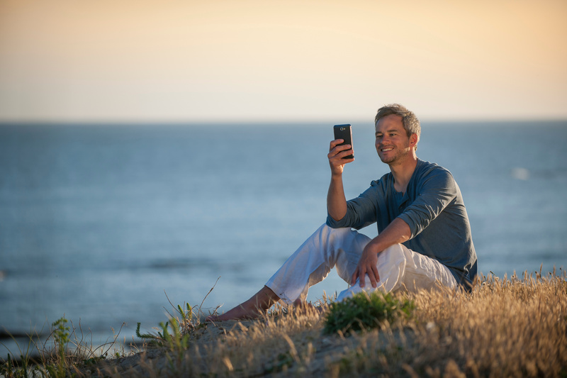 Mężczyzna siedzący na wydmie nad morzem z telefonem w ręce