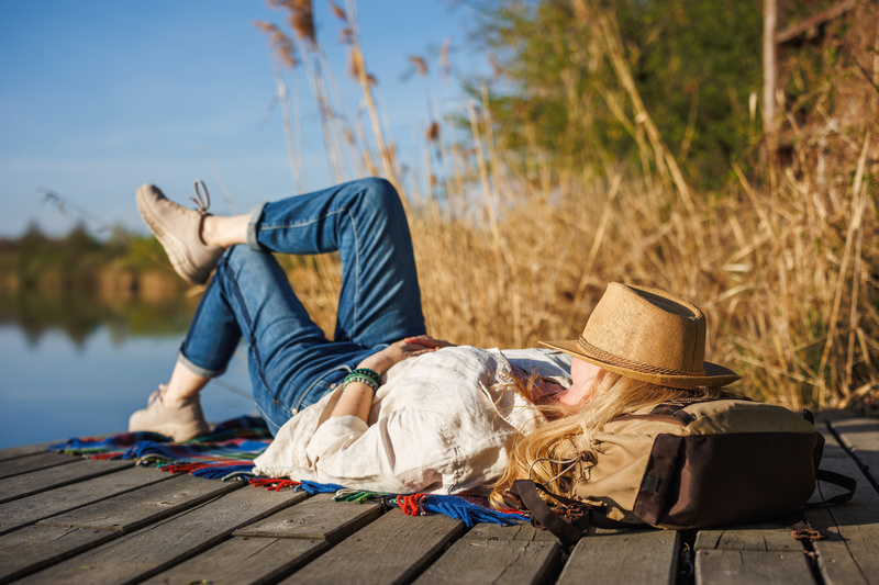 Kobieta leżąca na pomoście nad jeziorem z kapeluszem na twarzy