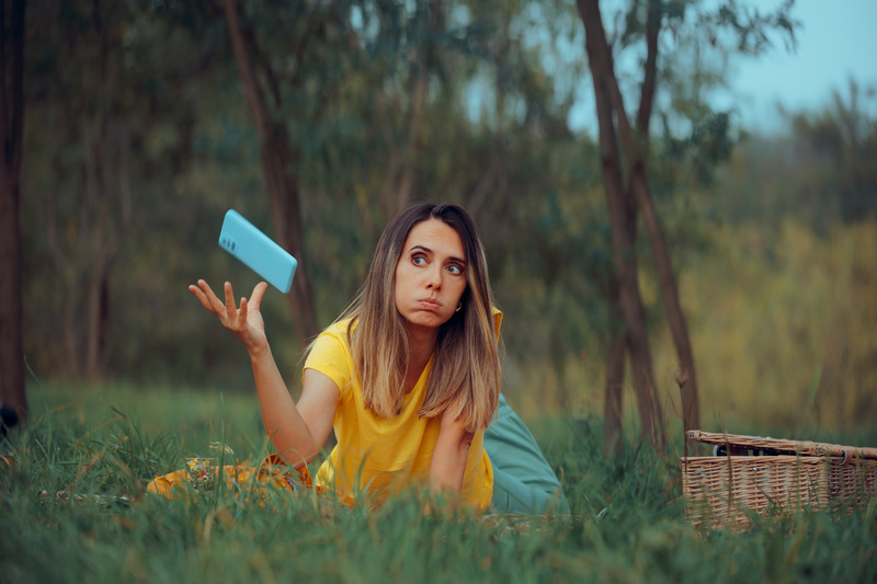 Kobieta leżąca na trawie podrzucająca smartfona