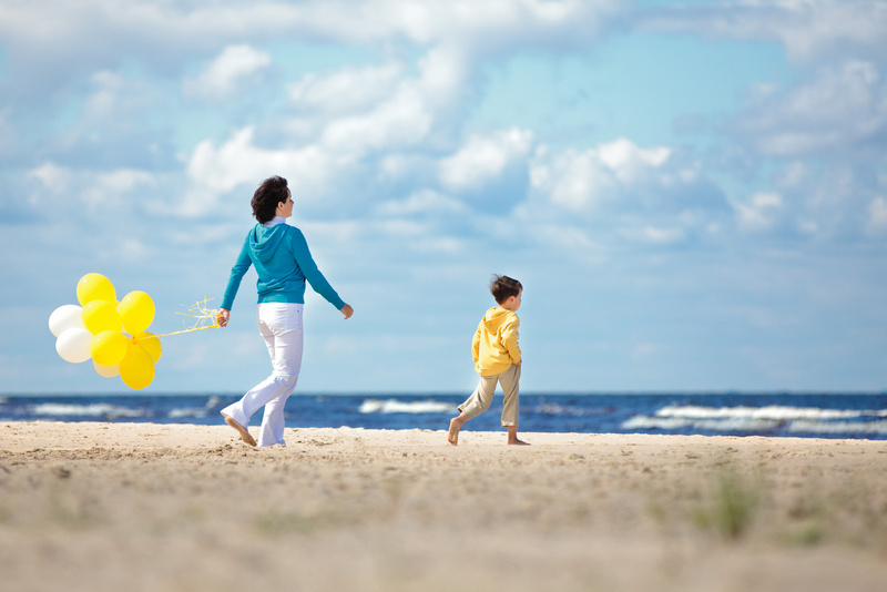 Mama z balonami w ręce i z chłopcem idącym przed nią po plaży