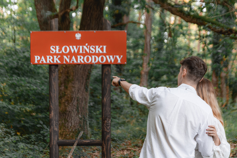 Para wskazująca palcem na tabliczkę z napisem Słowiński Park Narodowy