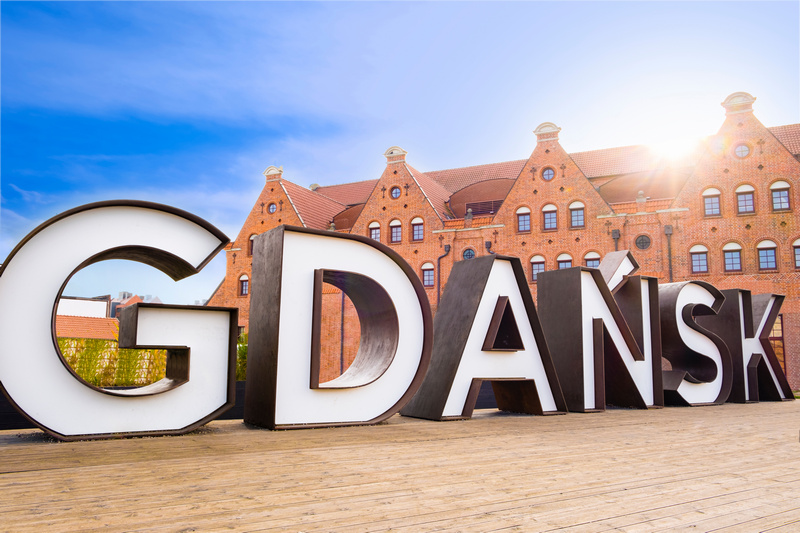 Stojący na ulicy na tle kamieniczek napis Gdańsk