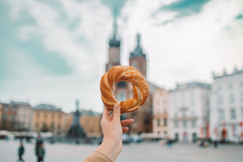 Kobieca dłoń trzymająca obwarzanka z krakowskim rynkiem w tle
