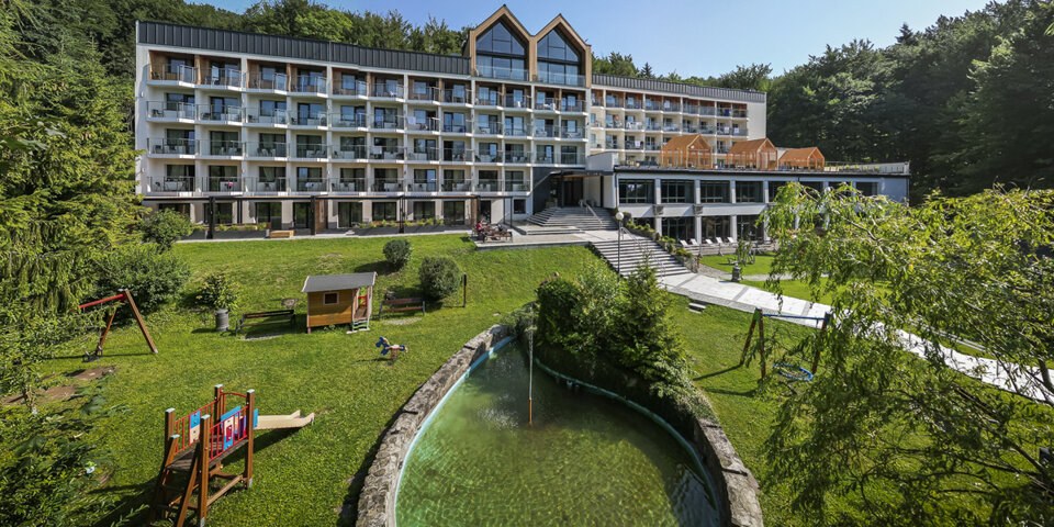 Hotel otacza zielony teren z placem zabaw i oczkiem wodnym
